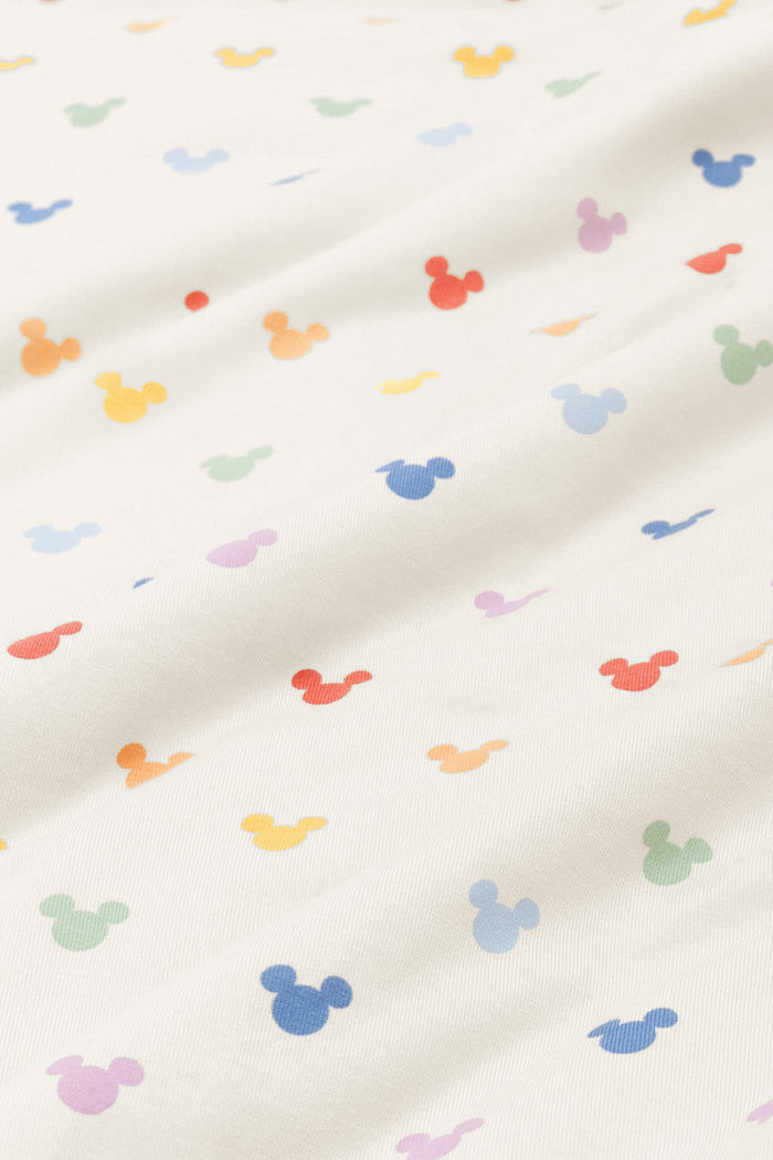 Close up of bamboo fabric swatch: An all-over print of classic Mickey Mouse heads in rows of pastel red, pastel orange, yellow, pastel green, sky blue, a muted blue, and a pinkish lilac, over a warm grey background color called Oat.