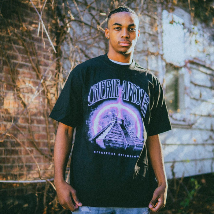 Someone wearing the Black Cherie Amour T-Shirt written above a pyramid with a purple ring of light surrounding the pyramid. Below the pyramid reads the words "Spiritual Ascension"