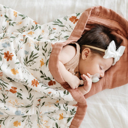 Baby girl wrapped cozily in a comfortable, multi-colored floral bamboo muslin quilt.