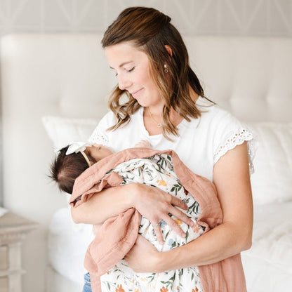 Mother holding daughter wrapped in a soft and cozy floral bamboo muslin quilt.
