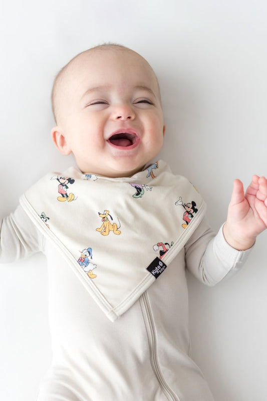 Baby wearing cream outfit with a Mickey Mouse and Friends printed bib