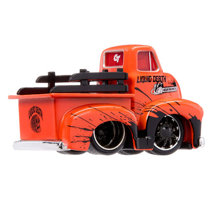 A die-cast toy model of a vintage pickup truck in bright orange with black splatter graphics, black tires, and 'Liquid Death' branding on the side and bed.