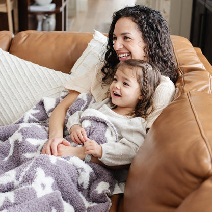 A mother sits with her little girl and a double-layer Bamboni® blanket. The plush, breathable blanket features a two-tone purple and white floral design, offering ultimate softness and warmth. Made from Saranoni’s signature stretchy, cloud-like Bamboni® fabric, this luxury baby blanket provides comfort for naps, tummy time, and on-the-go snuggles. The soft blanket is a receiving blanket and Saranoni blanket.