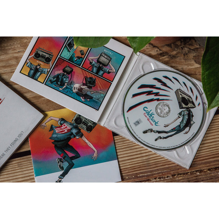 Open CD case with colorful comic-style artwork of a character with a boombox head, plus the Coldfront Collision CD and visible track list featuring Float Around and Natalie, all displayed on a wooden surface with green leaves.