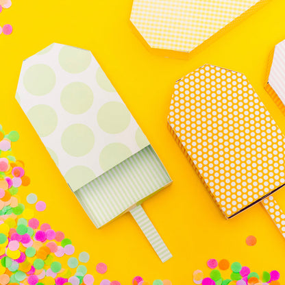 Decorative paper ice cream cones with polka dot patterns on a yellow background with colorful confetti.