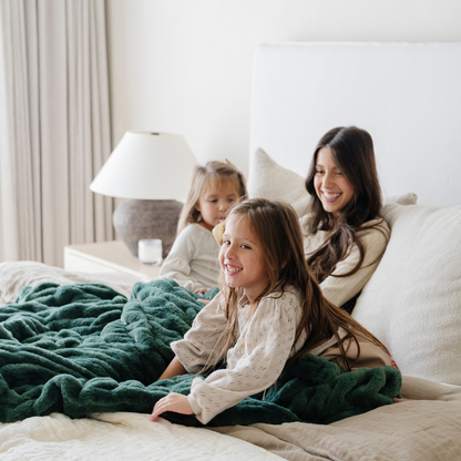 Smiling family cuddled together on a bed with a plush green double ruched holiday blanket, creating cozy family moments perfect for the winter season. Ideal for holiday decor and relaxation. The soft blanket is a luxury blanket.