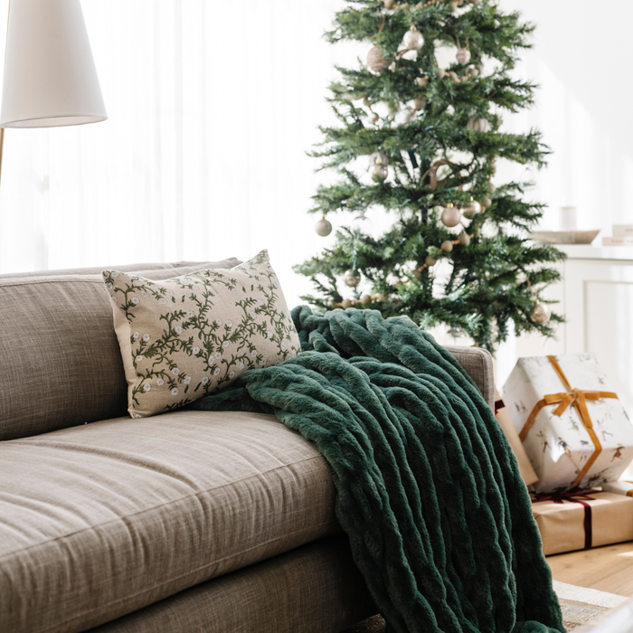Plush green double ruched blanket draped over a sofa beside a Christmas tree and presents, creating a cozy, festive atmosphere in the living room. Ideal for holiday home decor and winter warmth. The soft blanket is a luxury blanket and a Saranoni blanket.