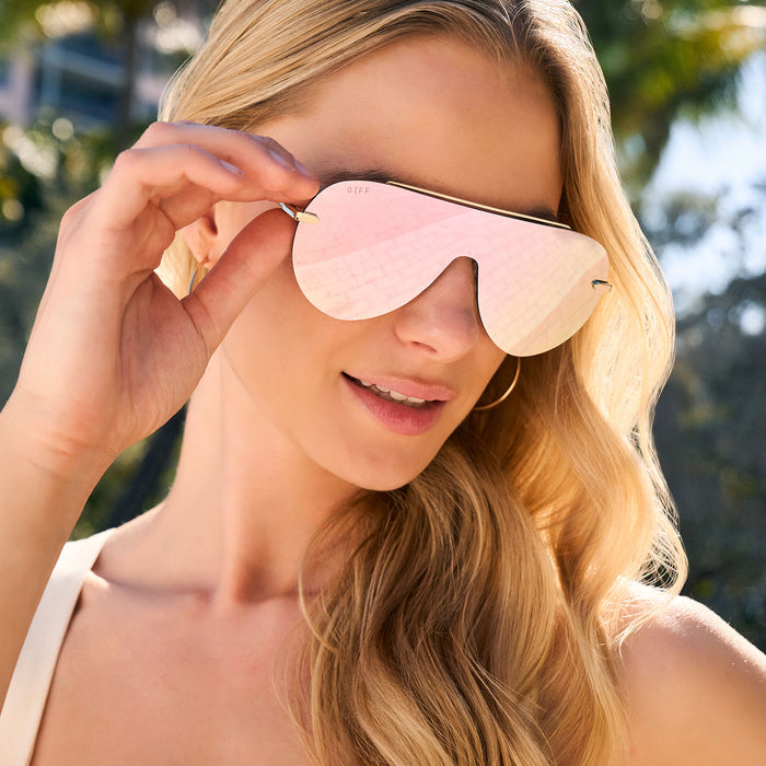 lifestyle - female wearing diff eyewear featuring the imani shield sunglasses with a gold frame and cherry blossom mirror lenses