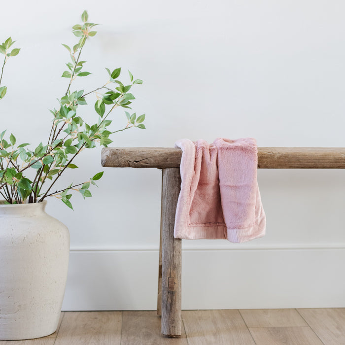 A Mini Saranoni Lush Blanket that is light pink is draped over a wood bench.