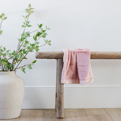 A Mini Saranoni Lush Blanket that is light pink is draped over a wood bench.