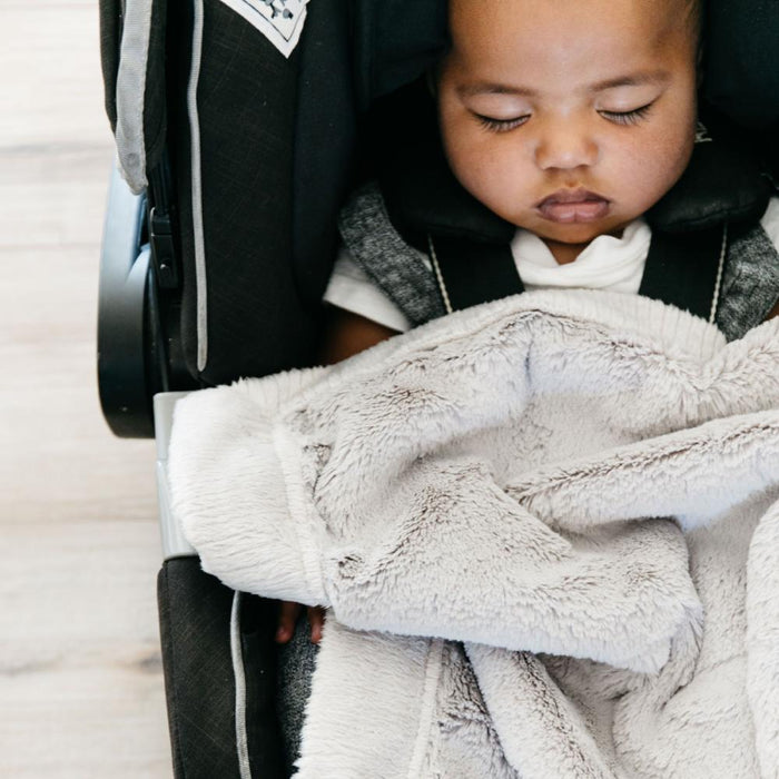 Baby boy snuggled under a mini, neutral colored car seat blanket.