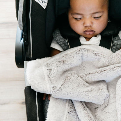 Baby boy snuggled under a mini, neutral colored car seat blanket.