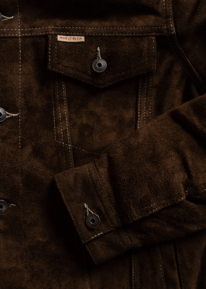 Close-up of a brown suede jacket with visible stitching and buttons, featuring an Iron & Resin label on the pocket flap.