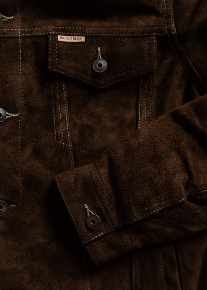 Close-up of a brown suede jacket with visible stitching and buttons, featuring an Iron & Resin label on the pocket flap.