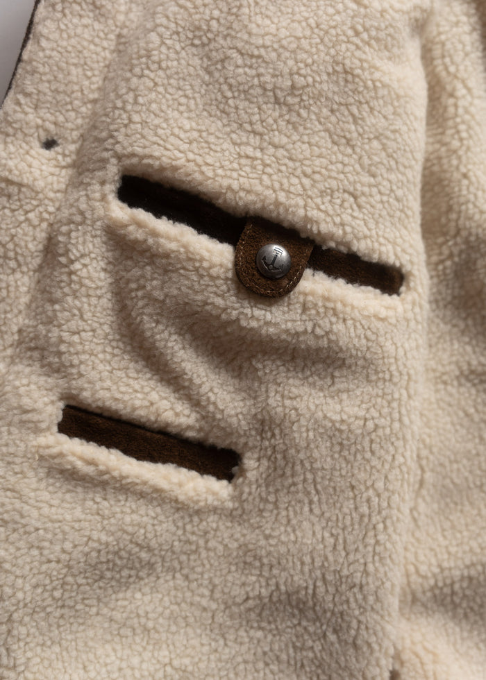 Close-up of a beige fleece jacket with two pockets and a metal button, showcasing its soft texture and cozy design.