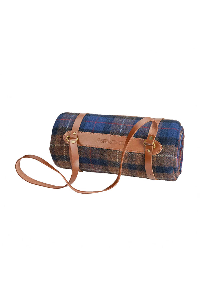 A rolled Pendleton blanket with blue plaid pattern, secured by brown leather straps and handle, ready for easy carrying.