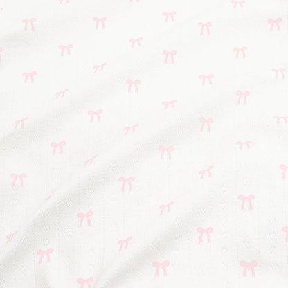 Close up of the pointelle fabric: An all-over print of dainty light pink bows over a white background.