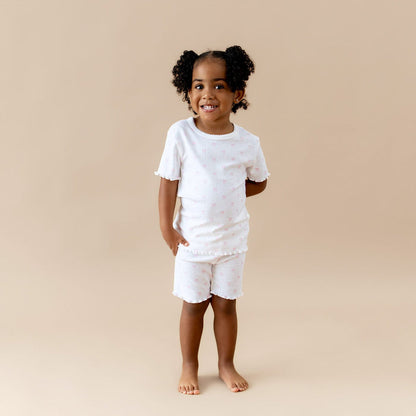 Young girl wearing a white outfit with pink bow print on a beige background