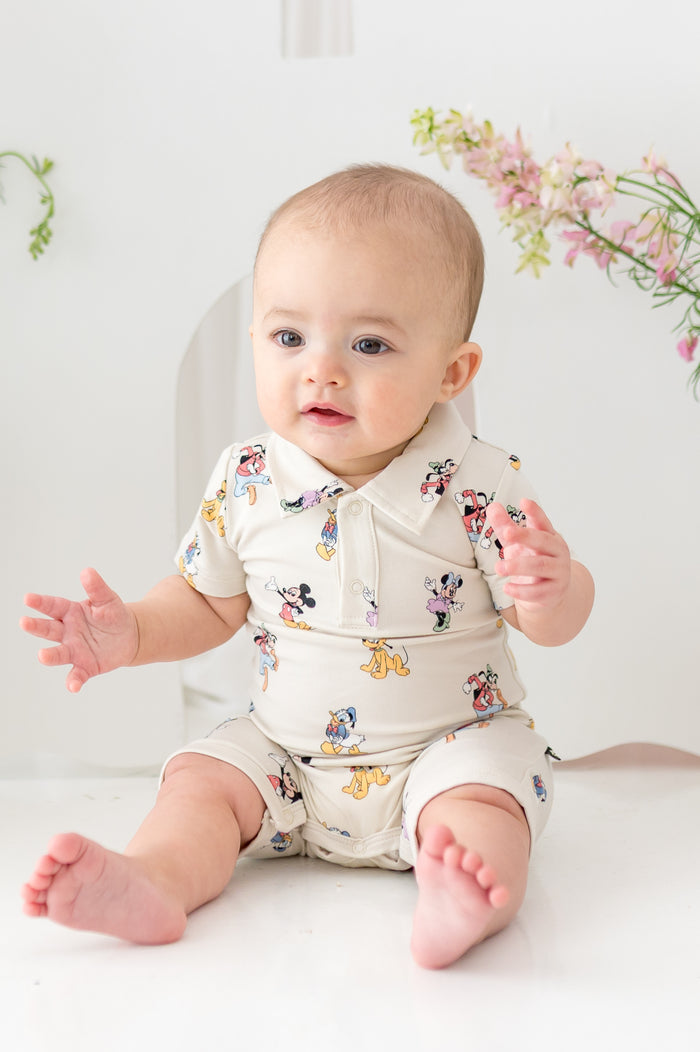 Baby sitting wearing a mickey and friends pattern shortall with polo collar
