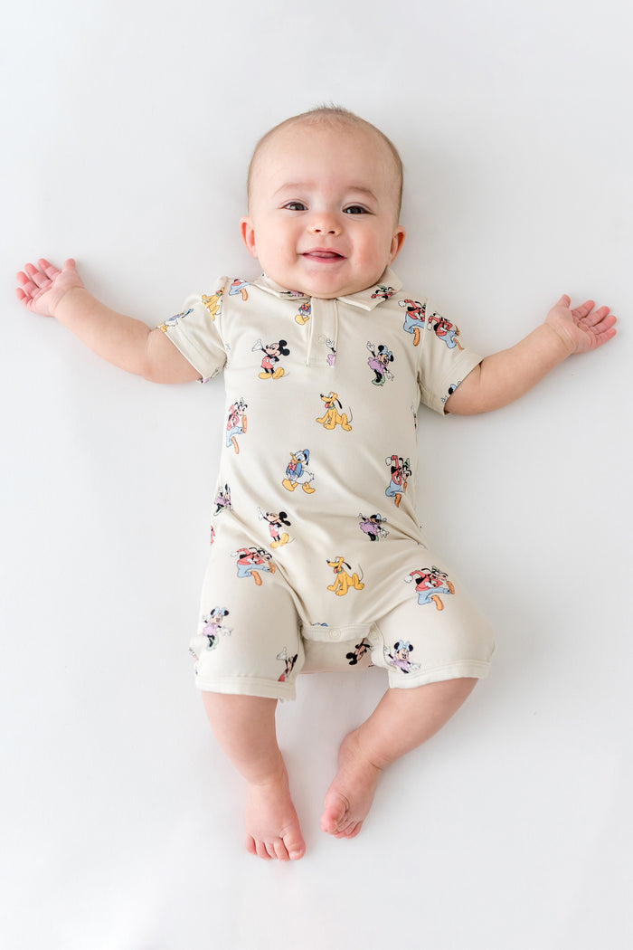 Baby in a polo shortall with mickey and friends pattern