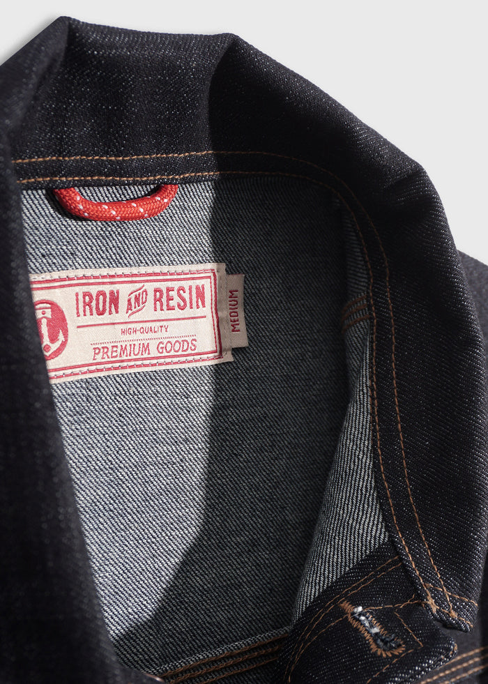 Close-up of a denim jacket's collar showing a red "Iron and Resin" label, highlighting its high-quality, premium goods.