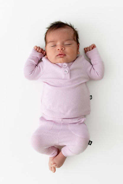 Sleeping newborn wearing the Ribbed Infant Henley Set in Thistle laying on a white surface