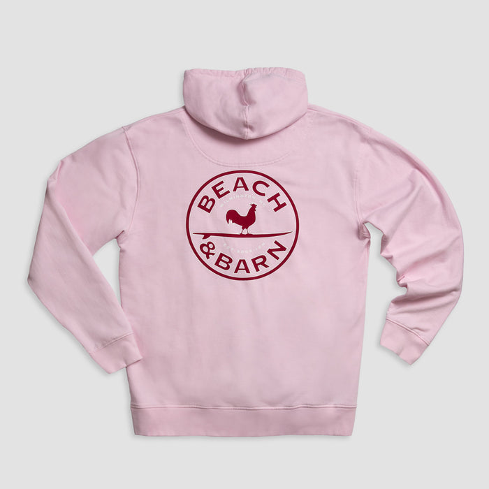 A light pink hoodie with a dark red circular logo on the back that reads BEACH & BARN and features a silhouette of a chicken in the center.