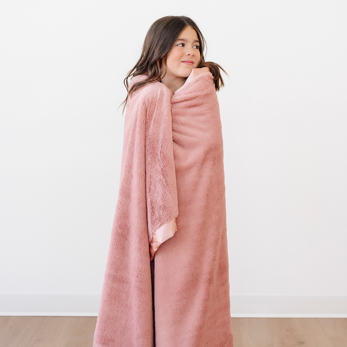 A little girl is wrapped in a lush blanket that is a peach blanket. This soft blanket is a luxury blanket and a Saranoni blanket. This adorable toddler blanket has a peach satin border as well. This cozy blanket is an adorable kid's blanket.