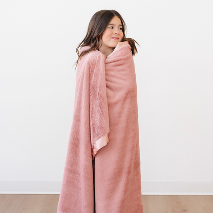 A little girl is wrapped in a lush blanket that is a peach blanket. This soft blanket is a luxury blanket and a Saranoni blanket. This adorable toddler blanket has a peach satin border as well. This cozy blanket is an adorable kid's blanket.