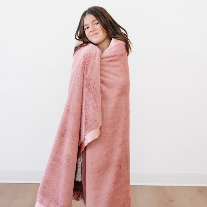 A little girl smiles and is wrapped in a Saranoni blanket that is a lush peach blanket with a peach satin border. This soft blanket is a luxury blanket and a toddler blanket. Enjoy this children's blanket. This cozy blanket is also a great toddler gift or little girl gift.