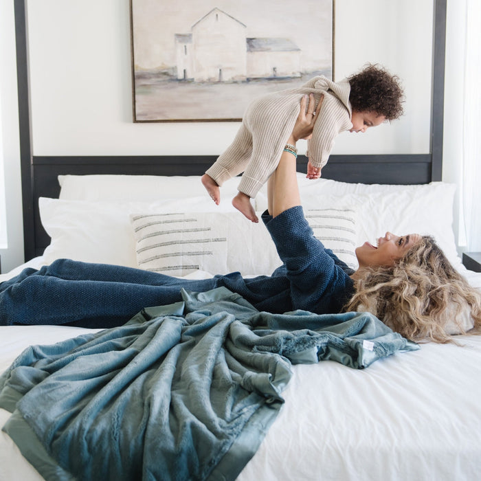 Mother and son playing together in bed laying on a teal toddler blanket.