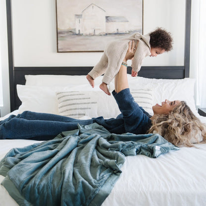 Mother and son playing together in bed laying on a teal toddler blanket.