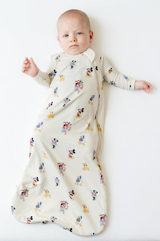 Infant laying on a light neutral surface wearing the Sleep Bag in Mickey Mouse and Friends 0.5 with matching romper