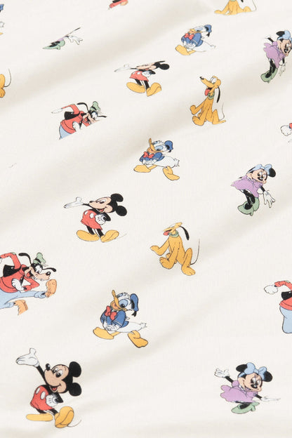 Close up of bamboo fabric swatch: An all-over print featuring: Mickey Mouse in his classic red shorts with white buttons and yellow shoes; Minnie Mouse wearing a blue headbow, a pink dress, and green heels; Goofy jumping in the air and wearing a green hat, a red shirt, blue pants, and orange shoes; Pluto wearing a green collar; and Donald Duck in his classic blue sailor outfit and hat, over a warm grey background color called Oat.