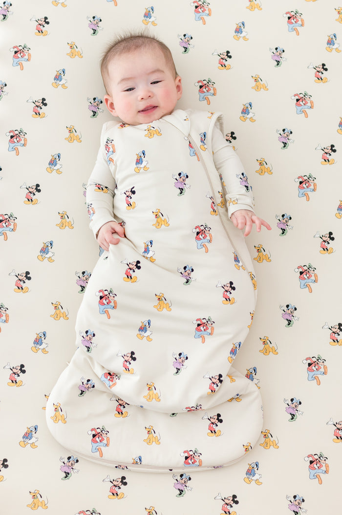 Baby in a crib with a Mickey Mouse and Friends pattern wearing a matching sleep sack