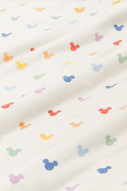 Close up of bamboo fabric swatch: An all-over print of classic Mickey Mouse heads in rows of pastel red, pastel orange, yellow, pastel green, sky blue, a muted blue, and a pinkish lilac, over a warm grey background color called Oat.