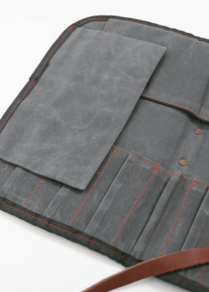 Gray canvas tool roll with red stitching, open to reveal multiple pockets and a flap, resting on a white surface.