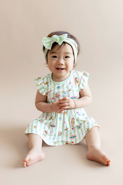 Child wearing a green and white striped twirl bodysuit dress with colorful Harry Potter patterns and a green headband on a beige background