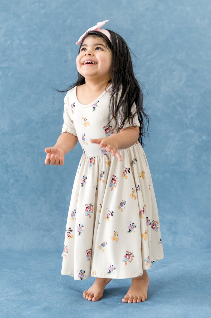 Girl wearing a cream twirl dress with mickey and friend pattern