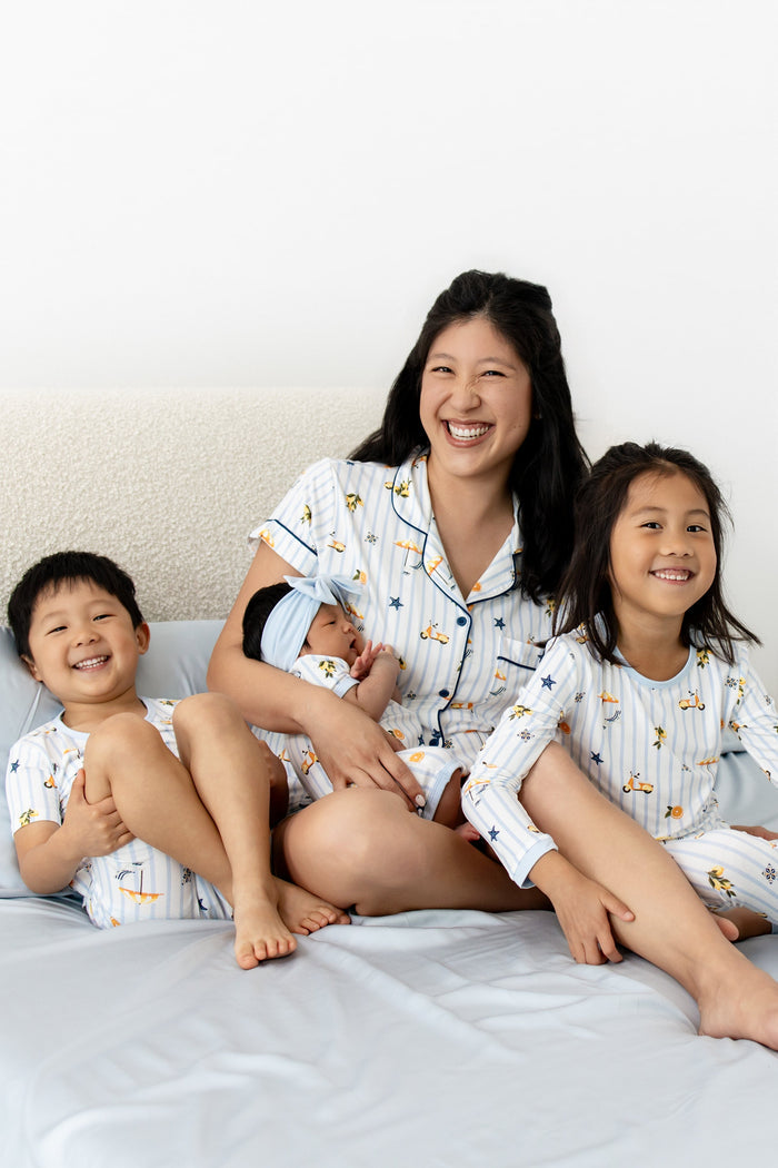 Family including a mom and 3 children wearing matching amalfi coast inspired pajamas on a bed with blue bedding