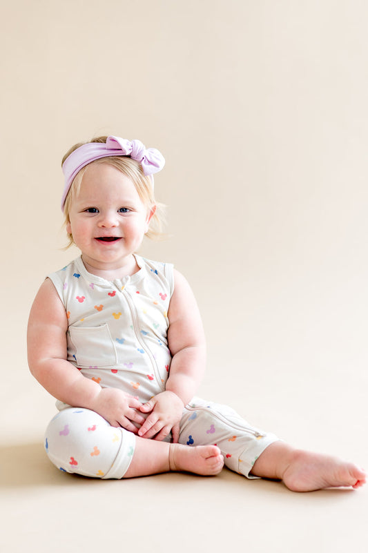 Baby sitting and wearing a zippered sleeveless romper in a colorful mickey head pattern